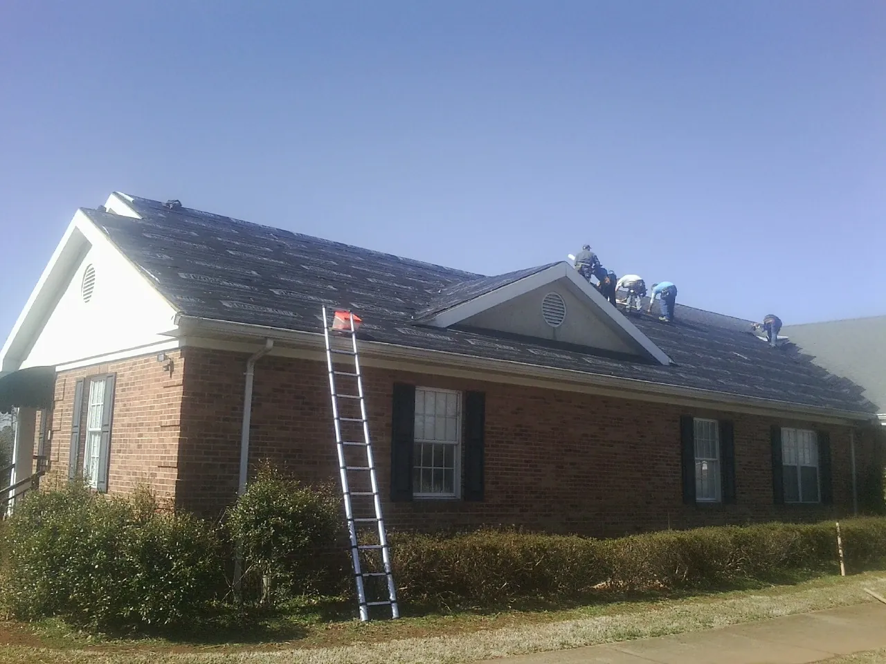 Crew tearing shingles off a brick ranch roof with a ladder set — Emergency Roof Repair work by our crew in Ojai