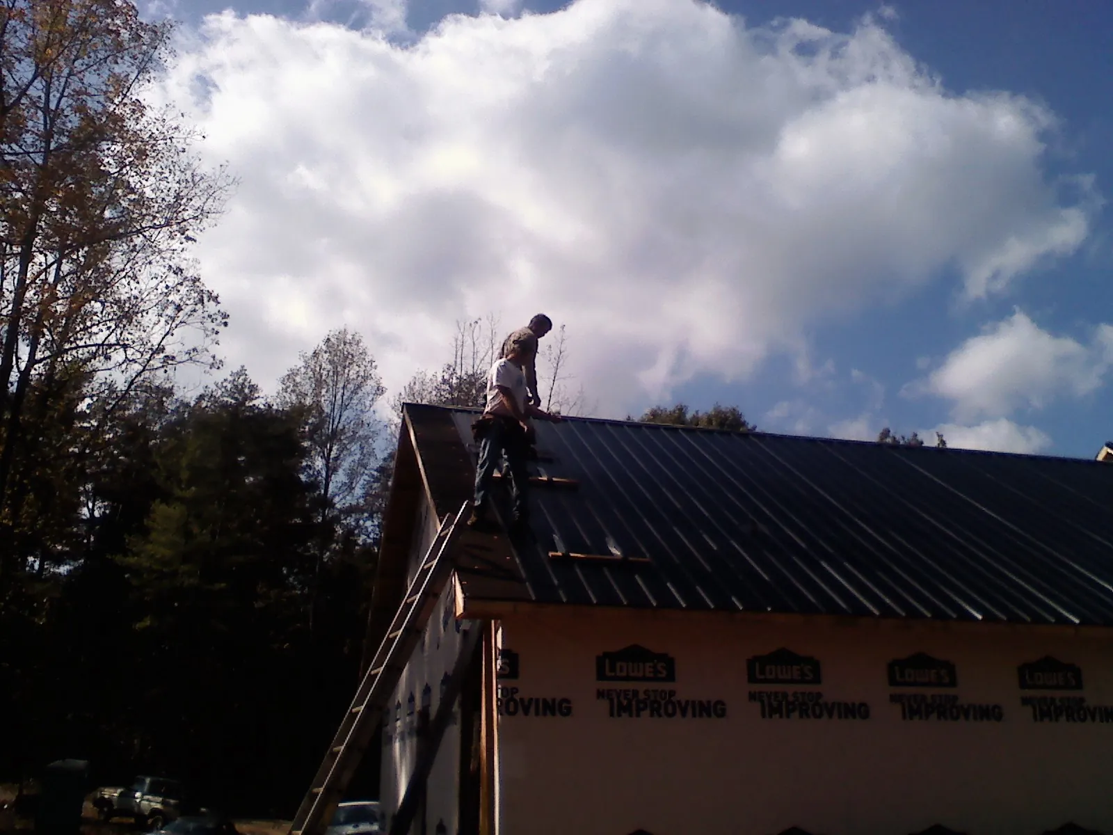 Roofer fastening dark metal panels high against a cloudy sky, from a Roof Inspection job in Ojai