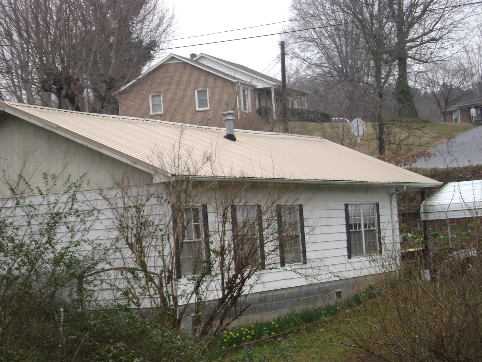 Tan metal roof on a white sided house set into a hillside — Commercial Roofing by Roofing Brothers in Ojai